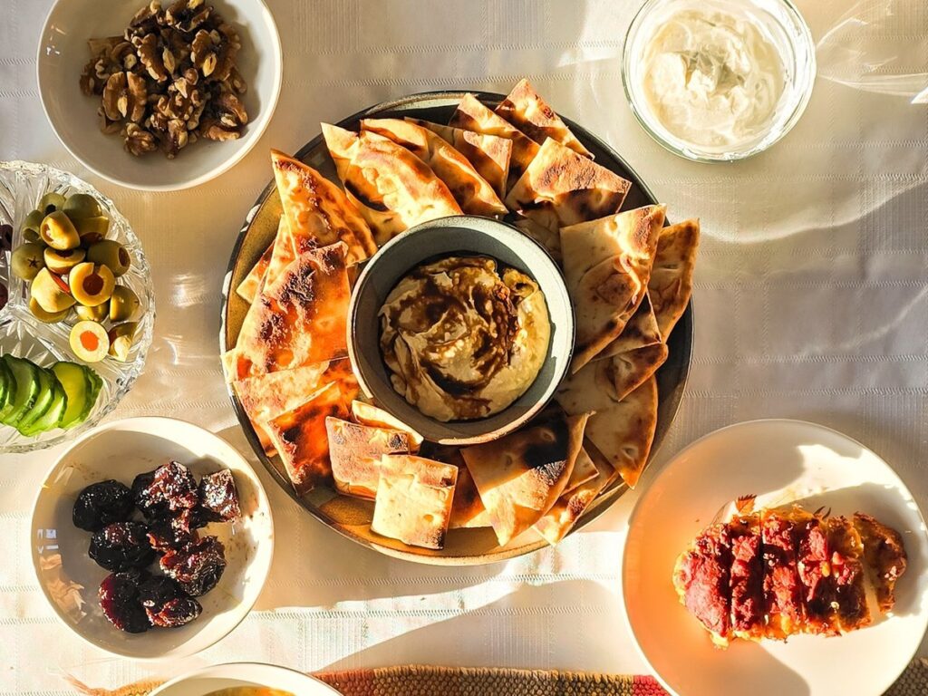 Mediterranean appetizer spread with warm pita bread, hummus, olives, dried fruit, walnuts, sliced cucumber, and soup, beautifully arranged on a table set for dinner.
