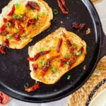 Overhead view of two slices of sourdough toast with sunny-side-up eggs cooked in the center, garnished with sundried tomatoes and chopped green onions, served in a black cast iron skillet on a woven placemat.