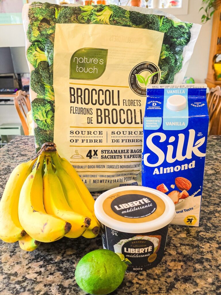 Fresh ingredients laid out for a healthy smoothie: Liberté key lime yogurt, Silk vanilla almond milk, bananas, a lime, and frozen broccoli—simple and nutritious.