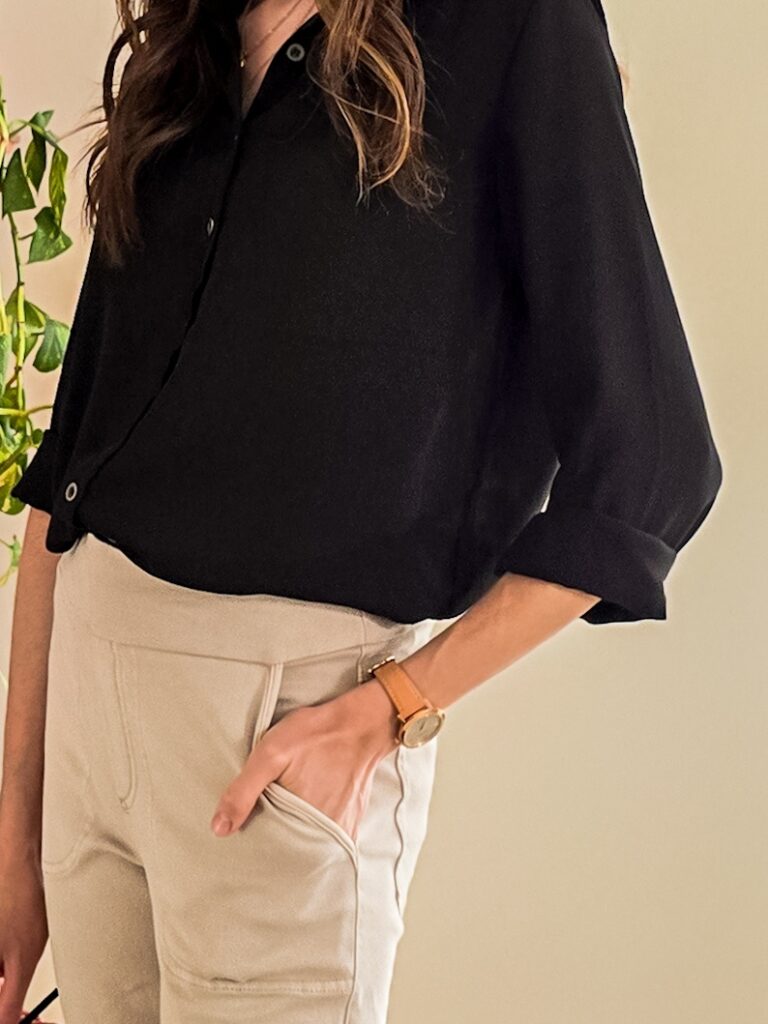 Close-up of a casual yet polished outfit featuring a tucked-in black button-up blouse and beige high-waisted pants with front stitching details.